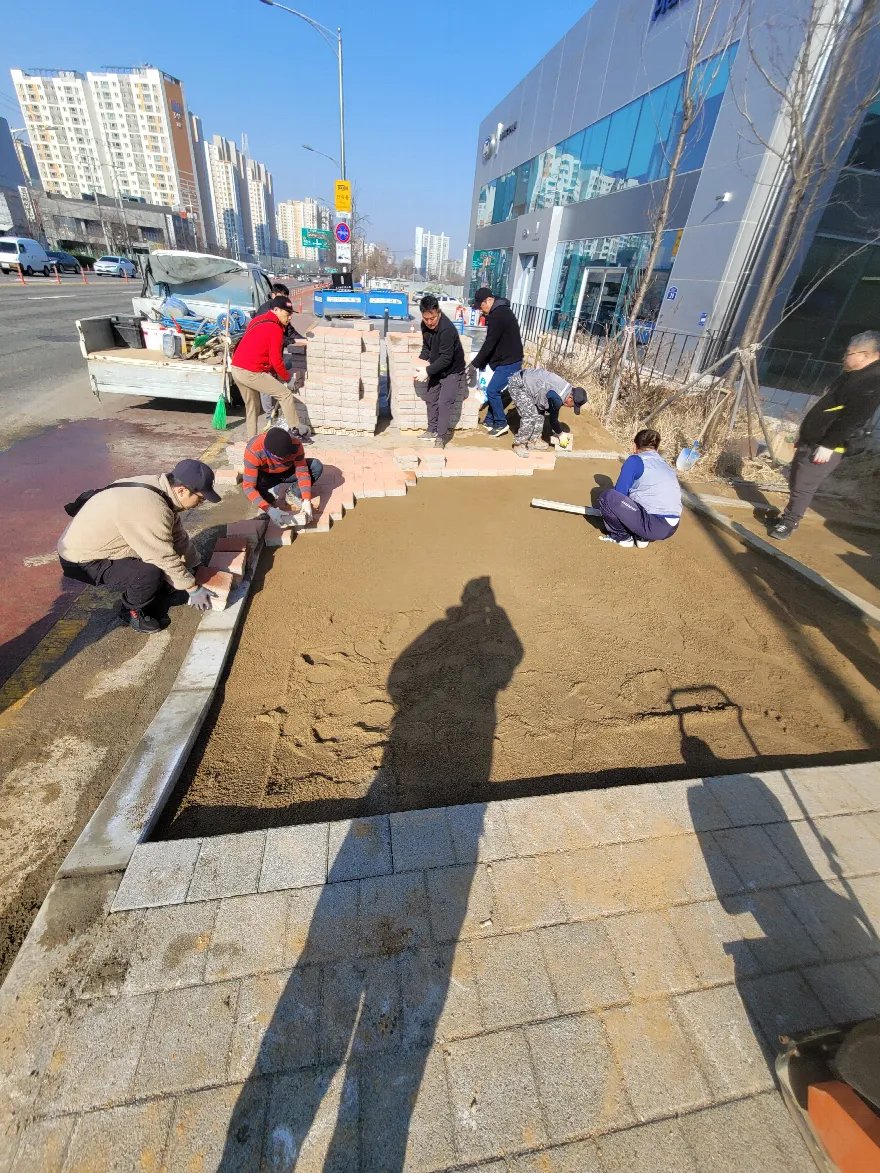 기층 모래를 평탄하게 포설한 뒤 여러 작업자가 동시에 블럭을 깔아 나가는 장면입니다.