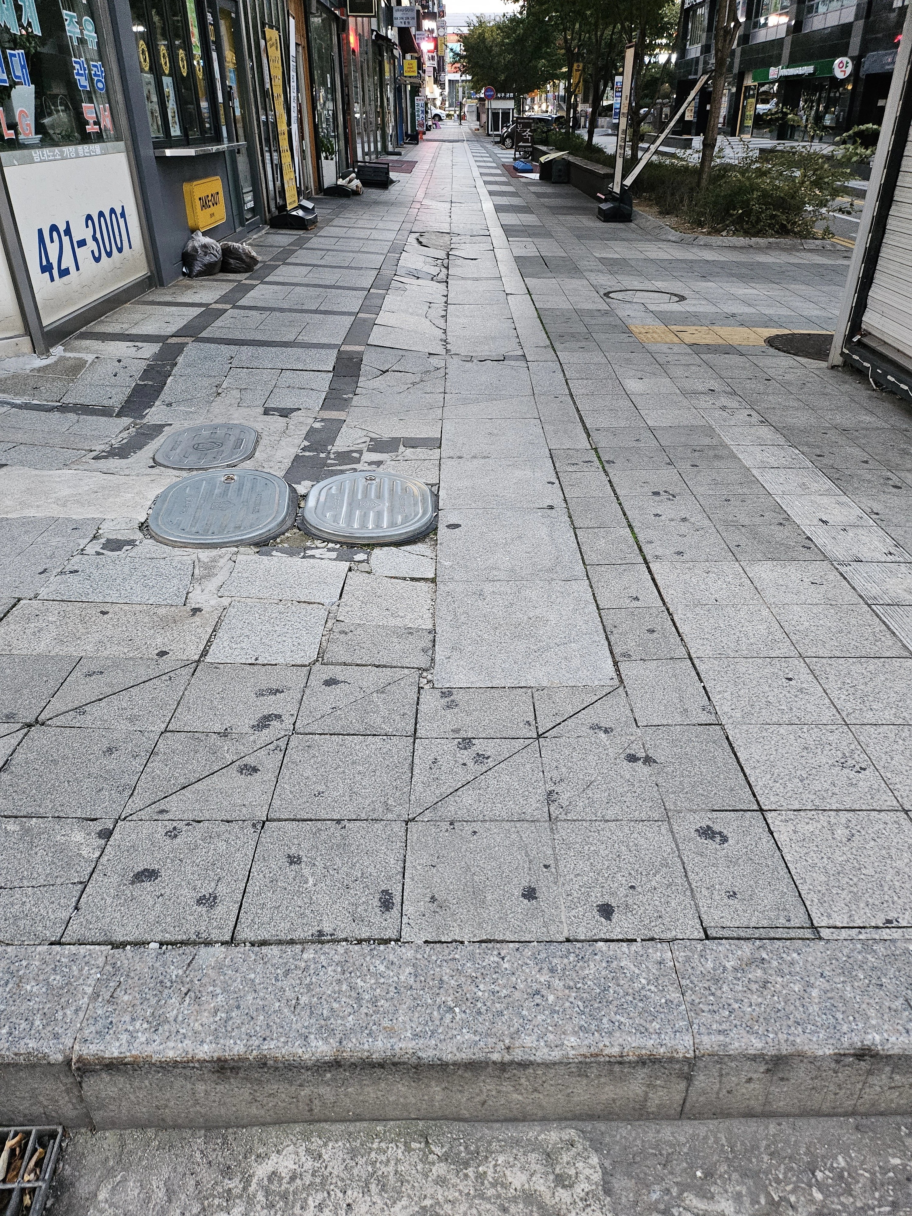 상가 앞 보도블럭 구간으로, 화강석 판석들 사이에 균열과 단차, 들뜸이 여러 군데 눈에 띕니다.