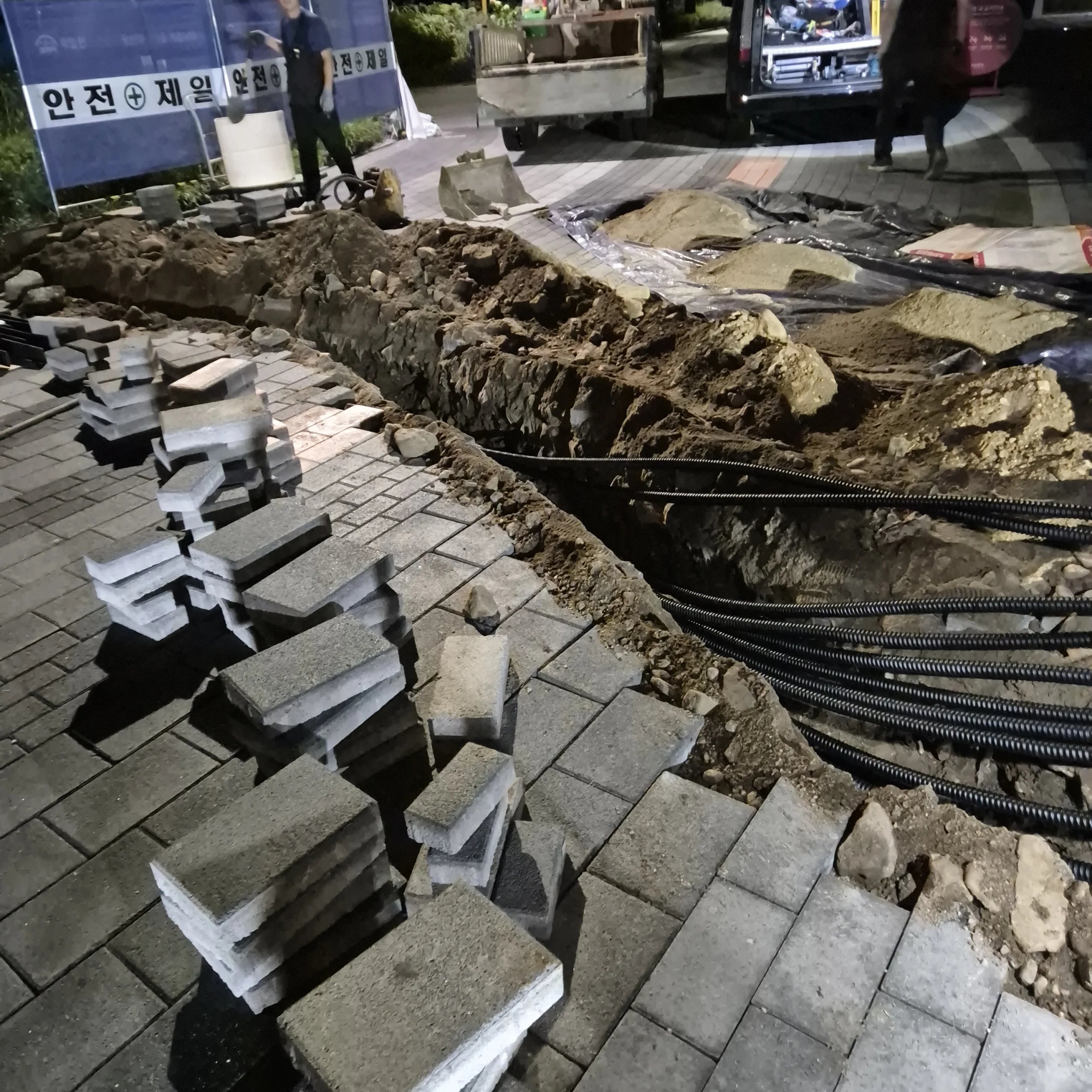 야간에 촬영된 사진으로, 보도블록을 길게 걷어내고 그 아래로 긴 트렌치(굴착 구간)가 드러나 있다.