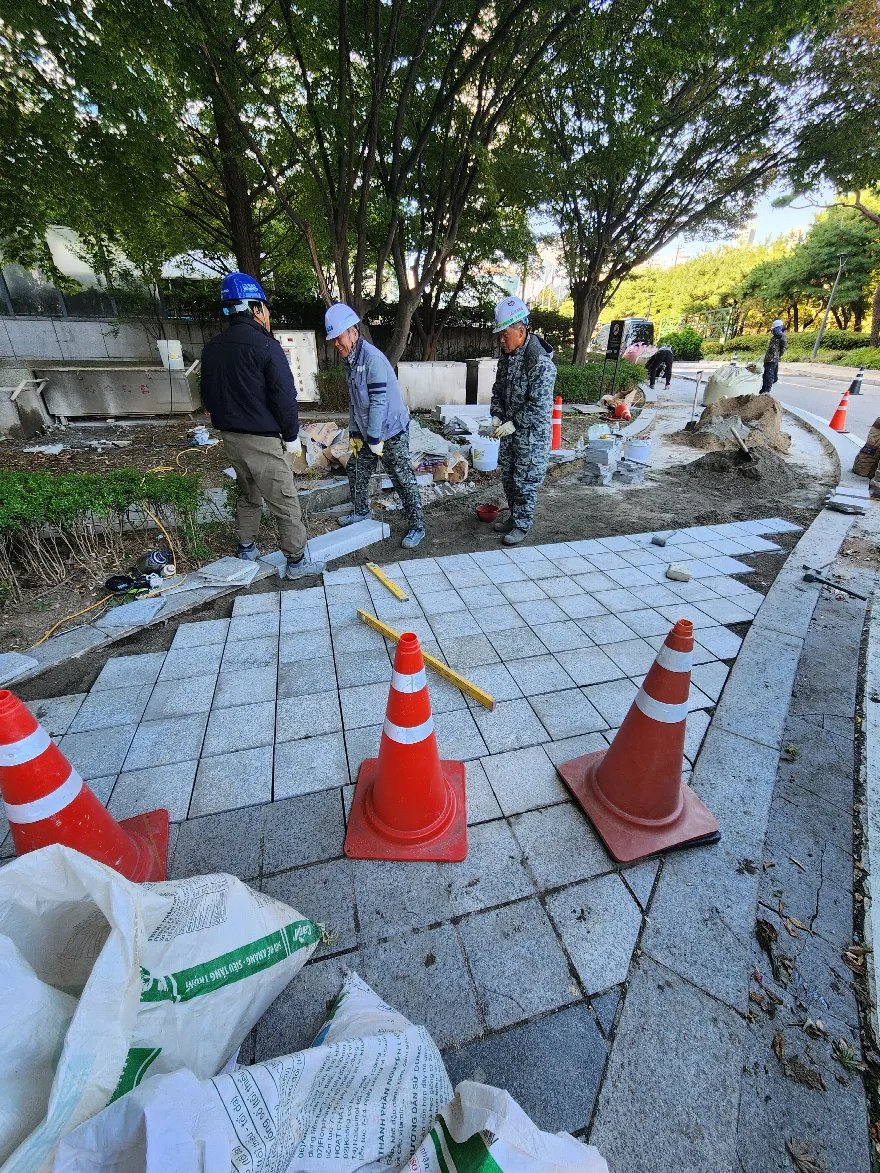 작업자 세 명이 화강석 판석 포장을 시공하고 있는 보도 현장입니다.