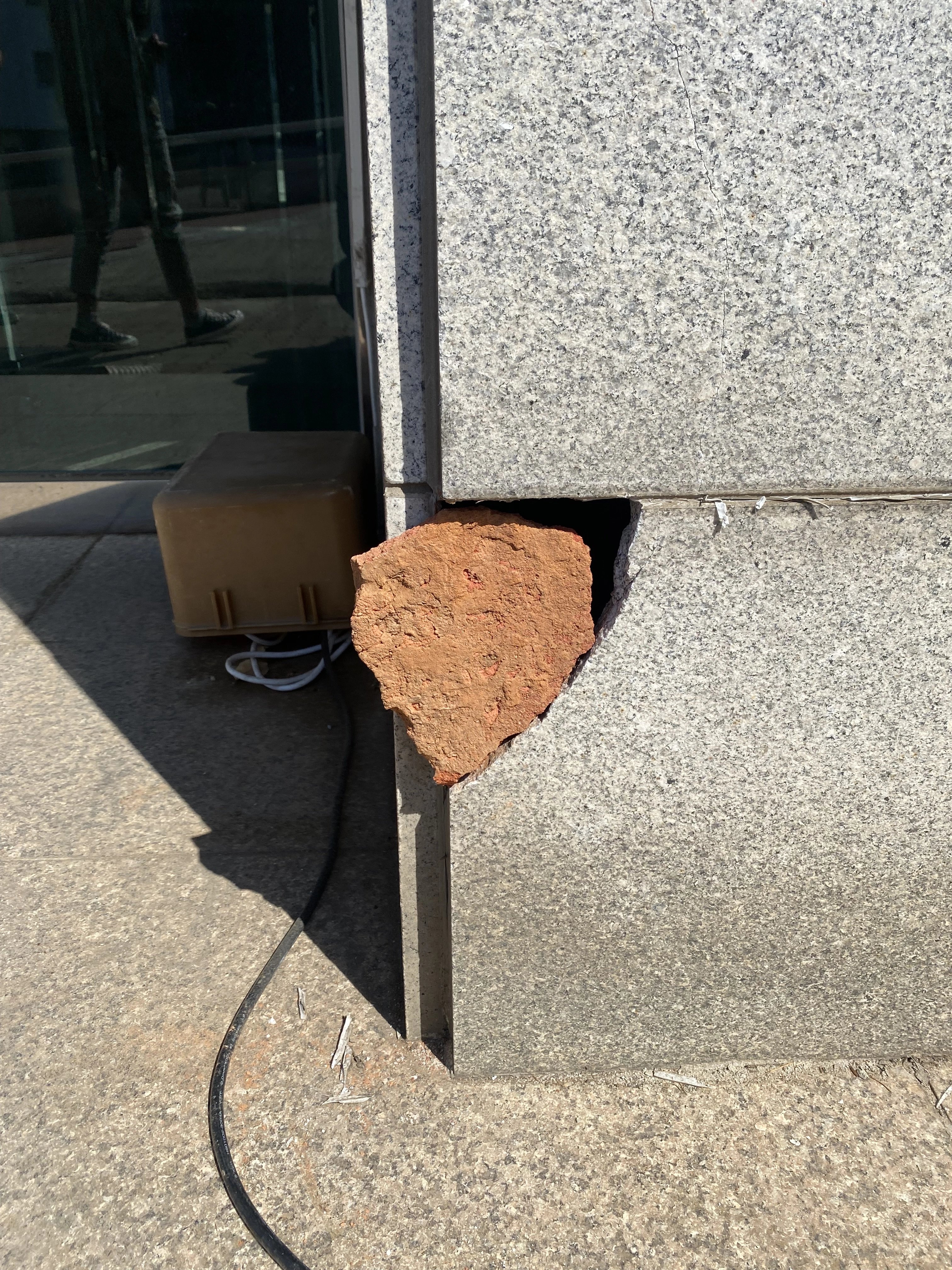 화강석으로 보이는 외벽 마감재 모서리 일부가 깨져 떨어져 나가 있고, 안쪽의 적갈색 바탕재(콘크리트 또는 벽돌 속채움)가 드러나 있습니다.