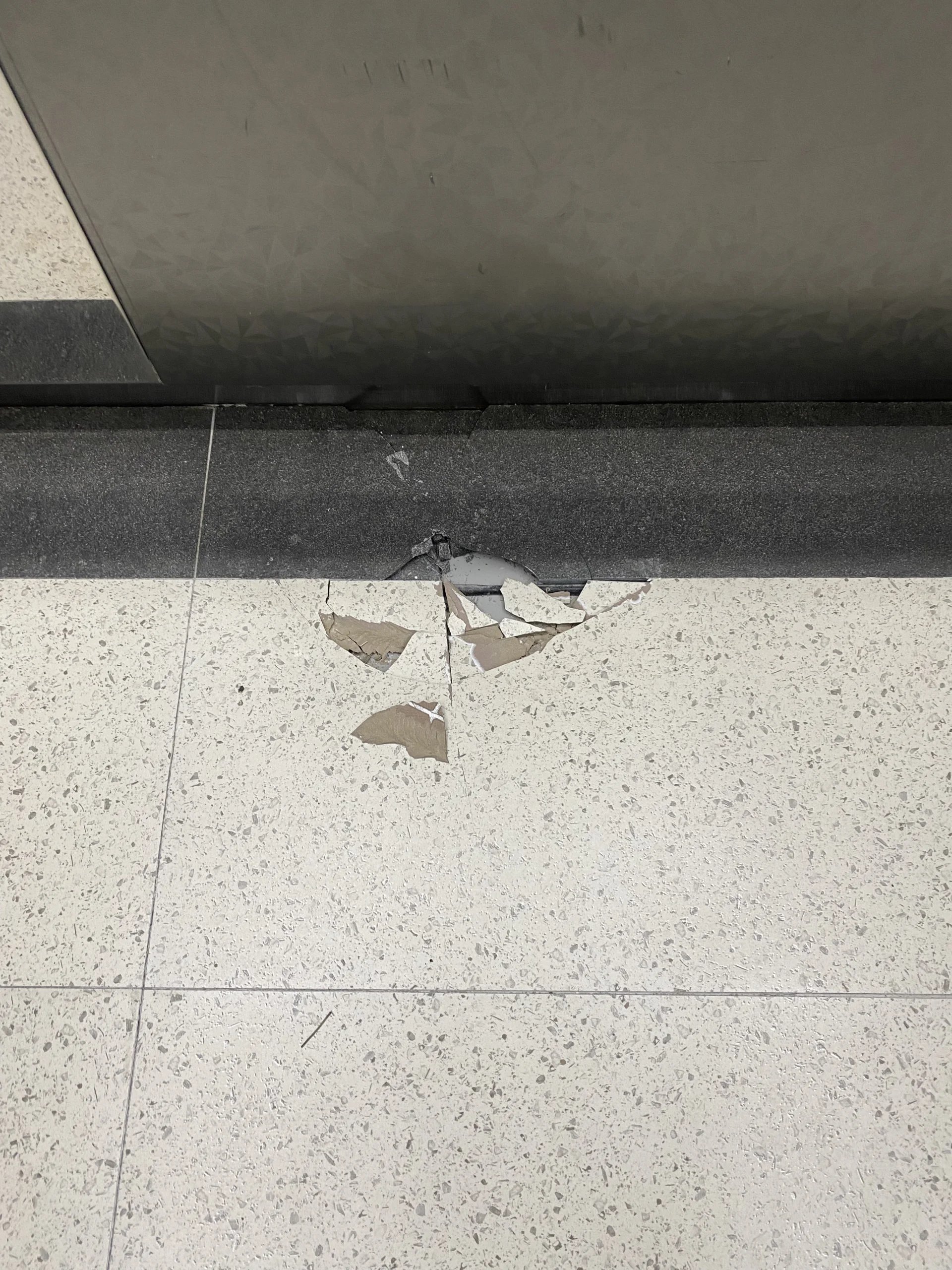 걸레받이 하단 바닥 타일(또는 판석) 모서리가 깨져 조각난 상태가 보입니다.