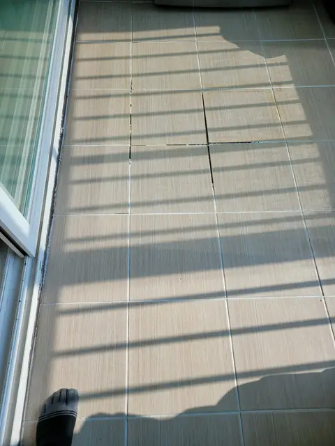블라인드 그림자가 드리운 창가 바닥에서 타일 모서리 한 곳이 깨져 떨어져 나가고 주변 줄눈은 고르게 남은 상태