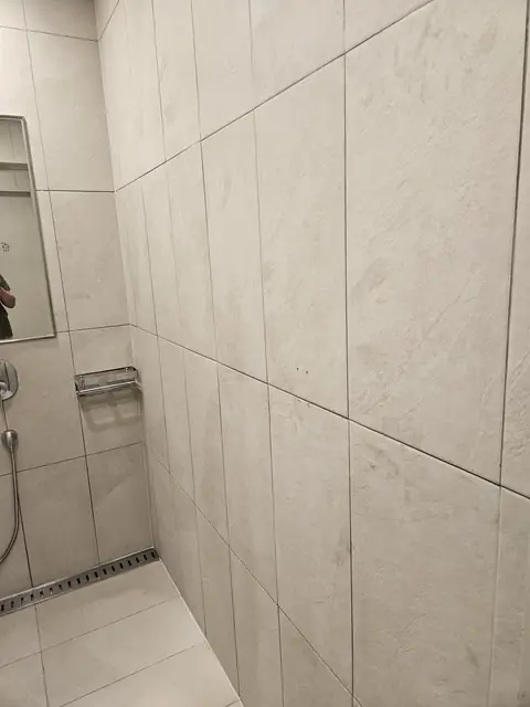 회색 대형 타일 샤워 공간 바닥에 스테인리스 커버 일자형 배수구가 벽선과 나란히 놓이고 그쪽으로 바닥이 기운 모습