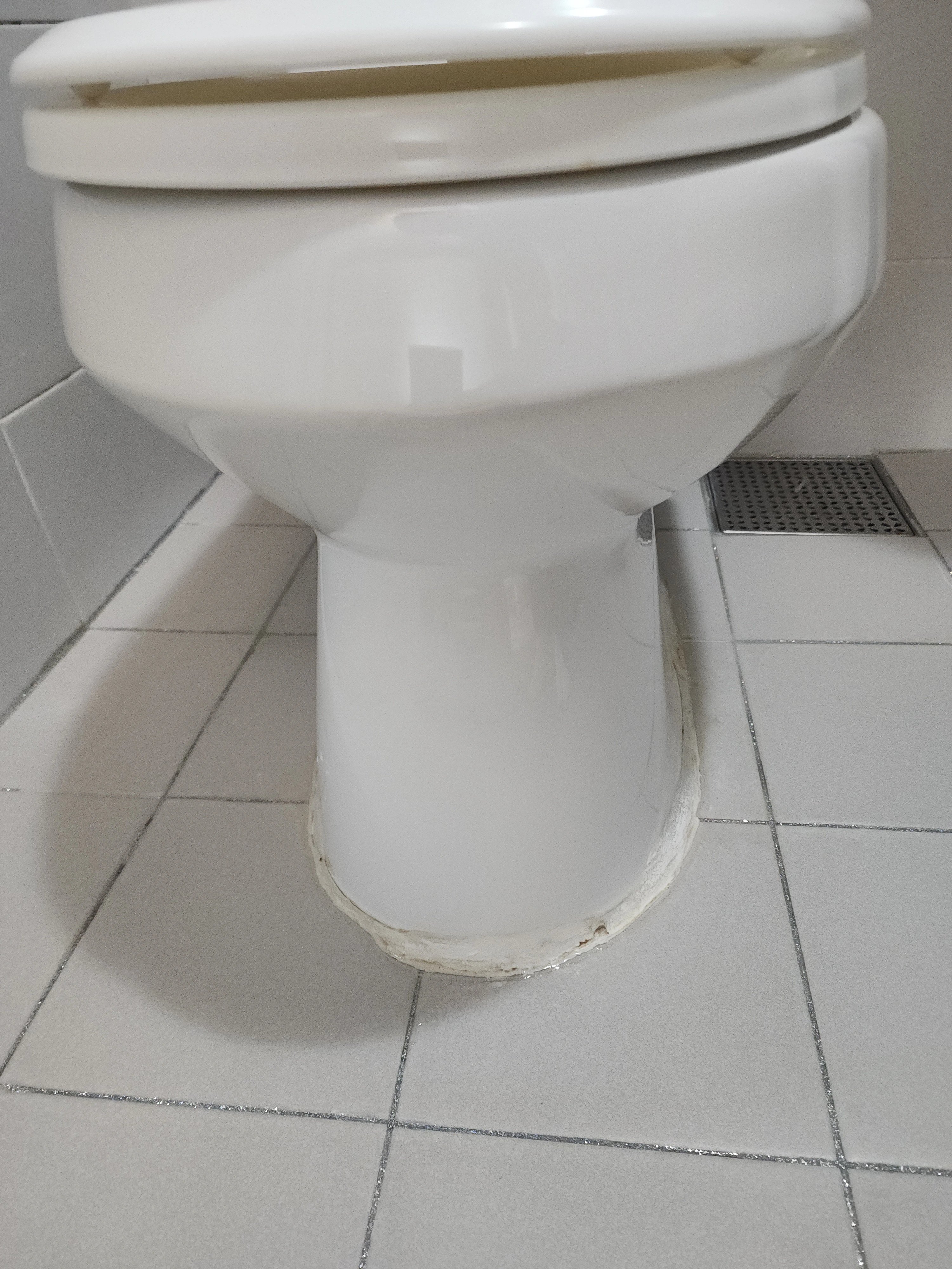 양변기 하단 마감 부위에 흰색 퍼티(실리콘 계열) 코킹이 둘러져 있는 모습입니다.