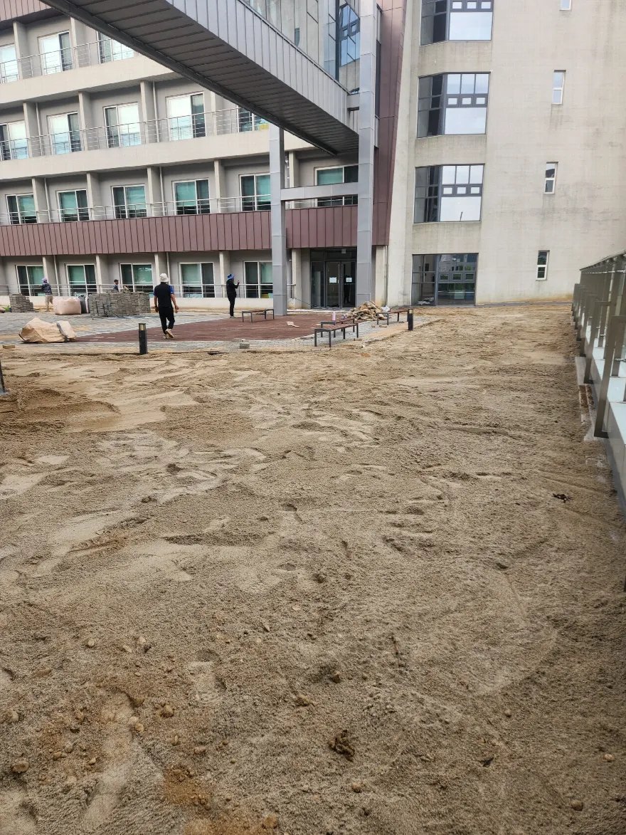 건물 앞 넓은 마당의 바닥을 걷어내고 마사토가 드러난 상태로, 장비 궤도 자국이 넓게 남아 있습니다.