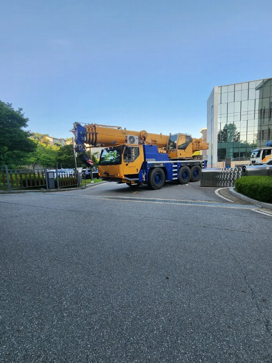 건물 앞 도로에 대형 크레인 차량이 들어와 주차되어 있는 장면입니다.