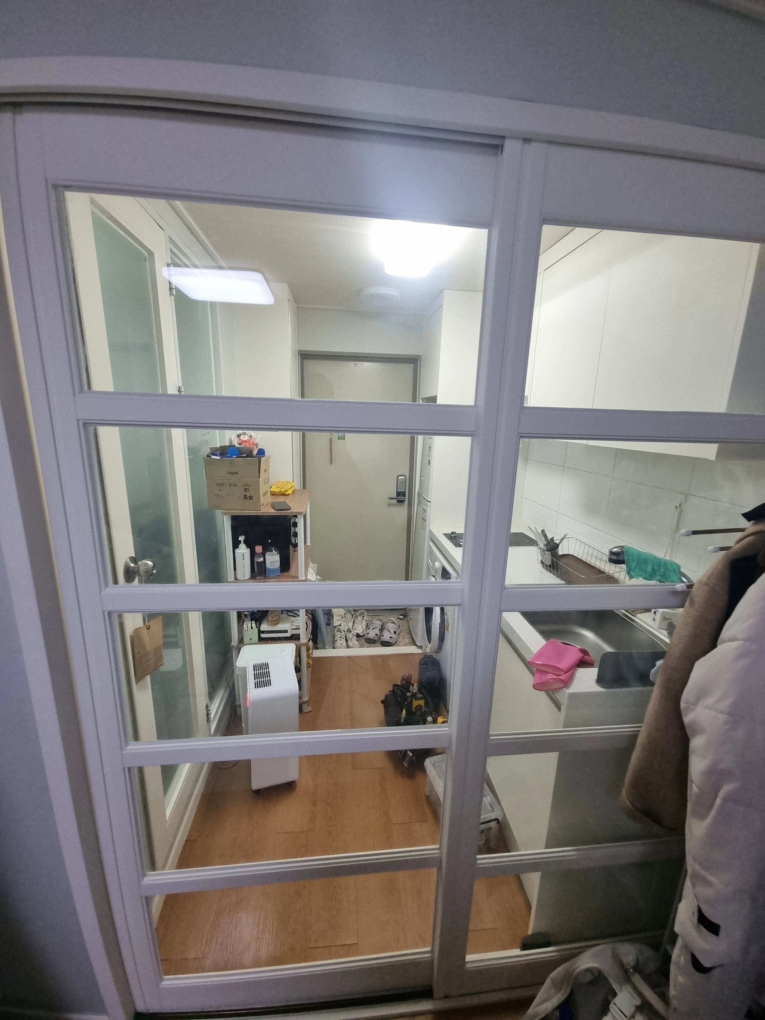 흰색 격자무늬 창틀 너머로 내부 복도와 주방 개수대가 보인다.